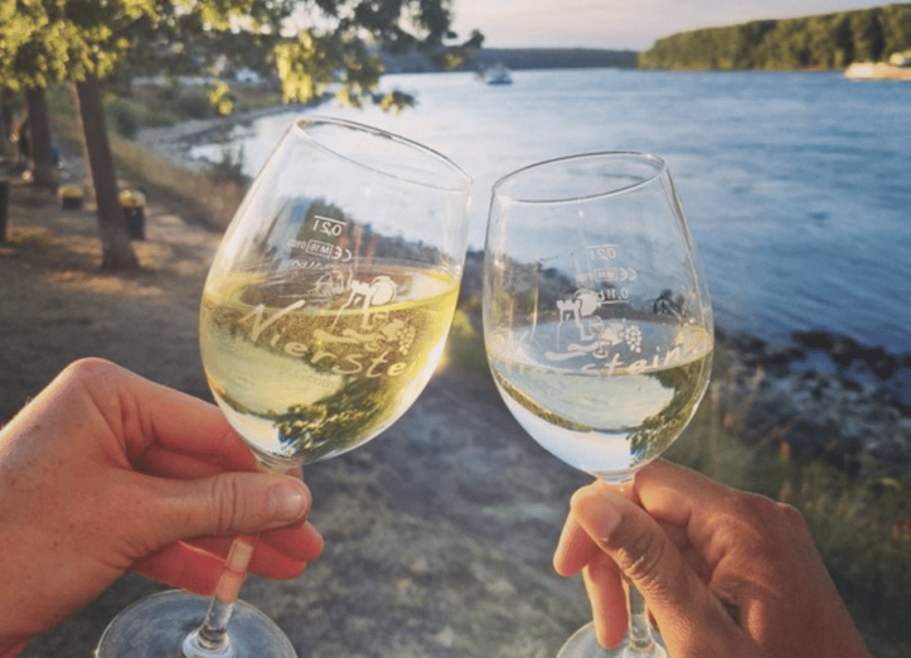 Zwei Gläser Niersteiner Wein stoßen vor dem Rhein an