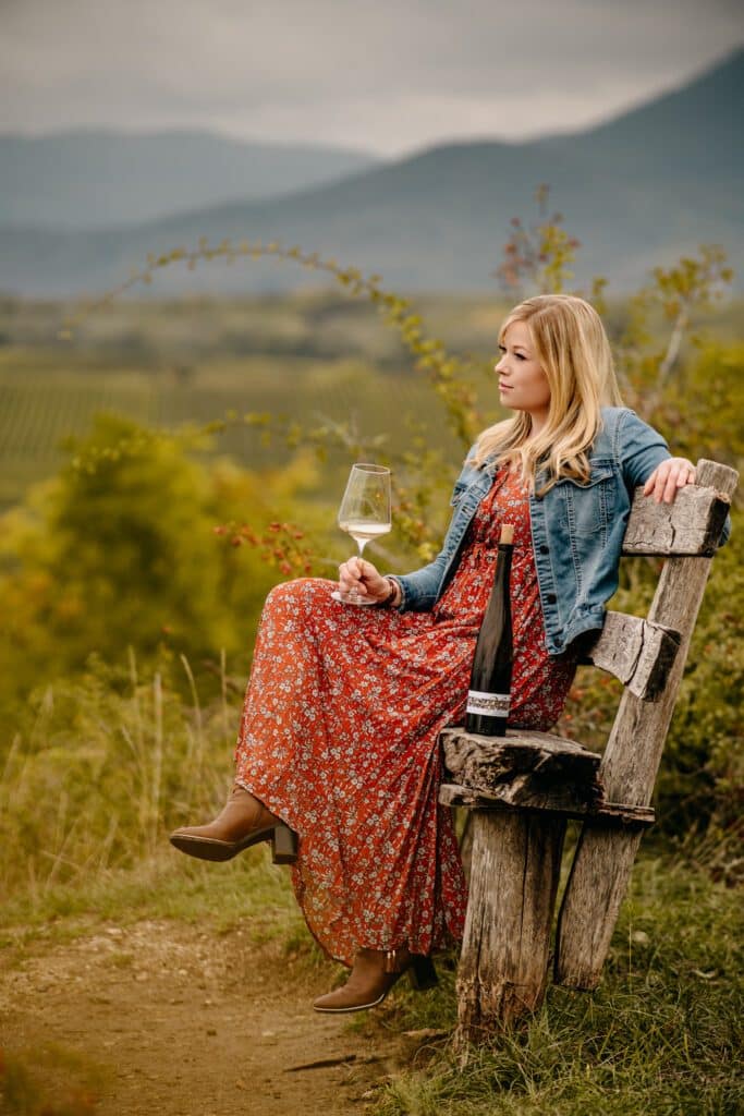 Jungwinzerin Vera Keller mit einem Glas Weißwein vor der Aussicht auf die Weinberge des Weingut Keller